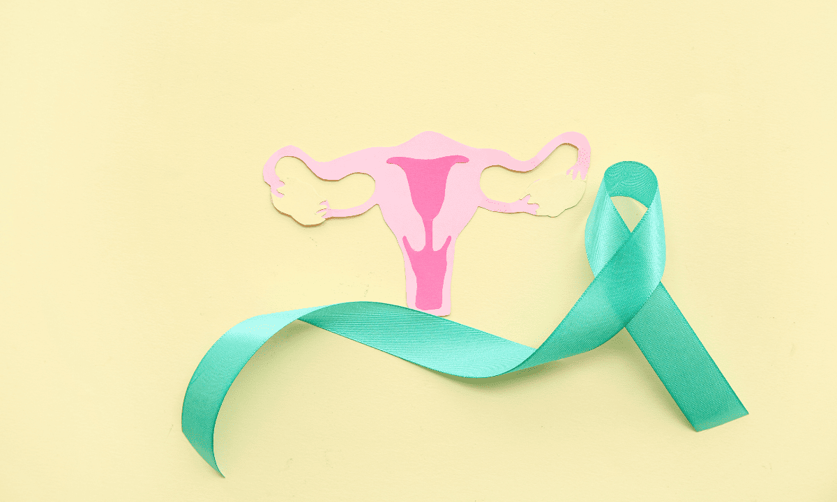 A pink paper cutout of the female reproductive system (uterus, ovaries, and fallopian tubes) next to a teal awareness ribbon on a yellow background.