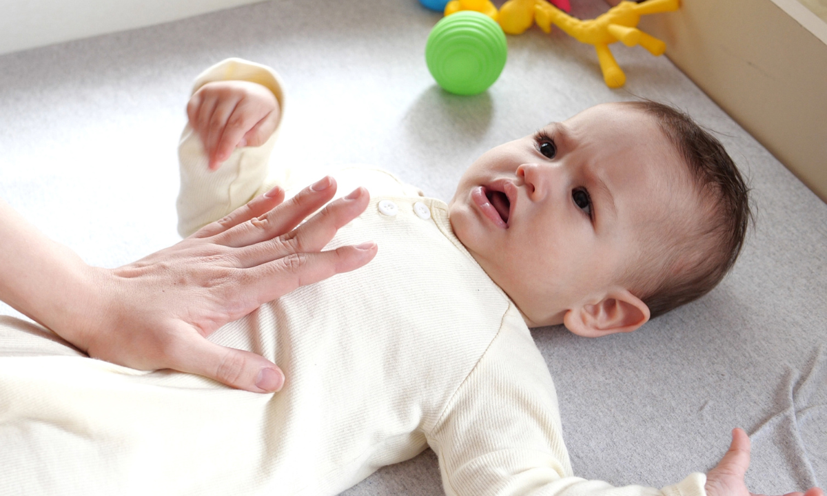 Adult hand gently pressing on the tummy of a crying baby.