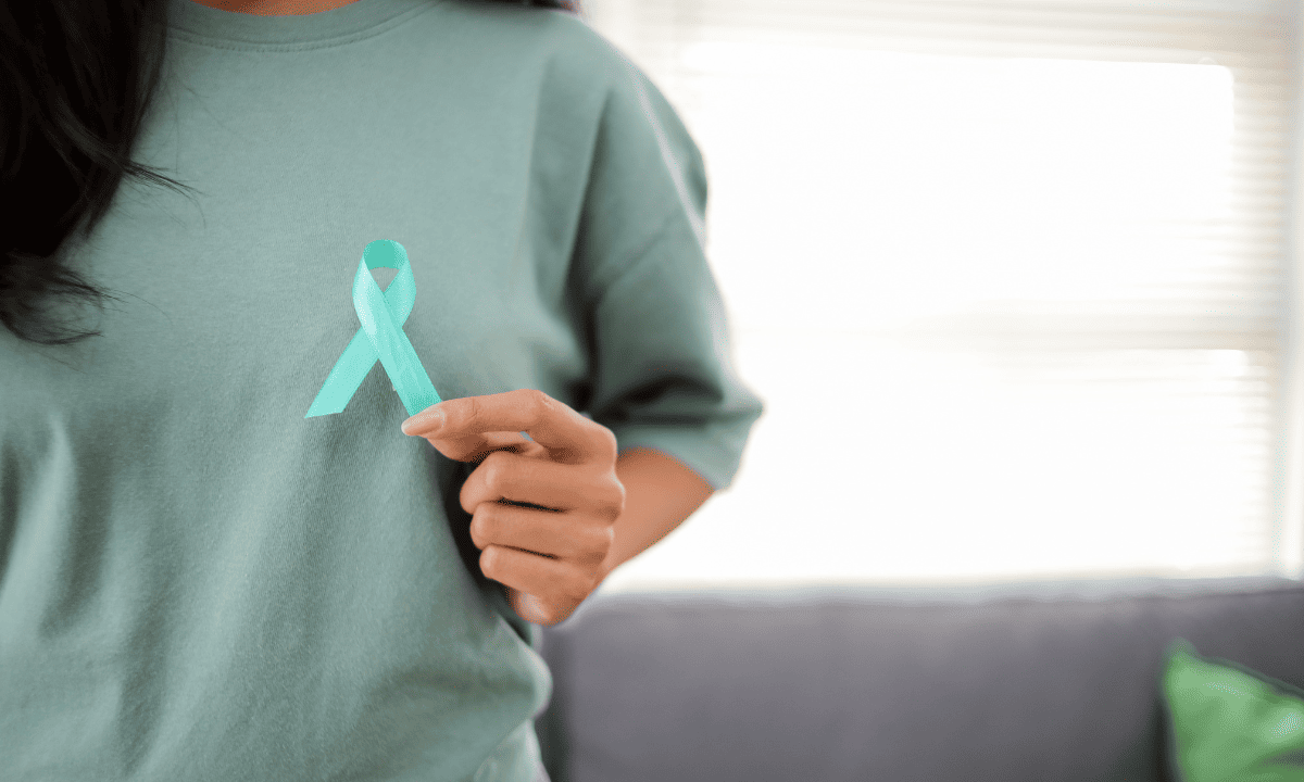 A person holding a teal ribbon against their chest, symbolizing support for cervical cancer awareness