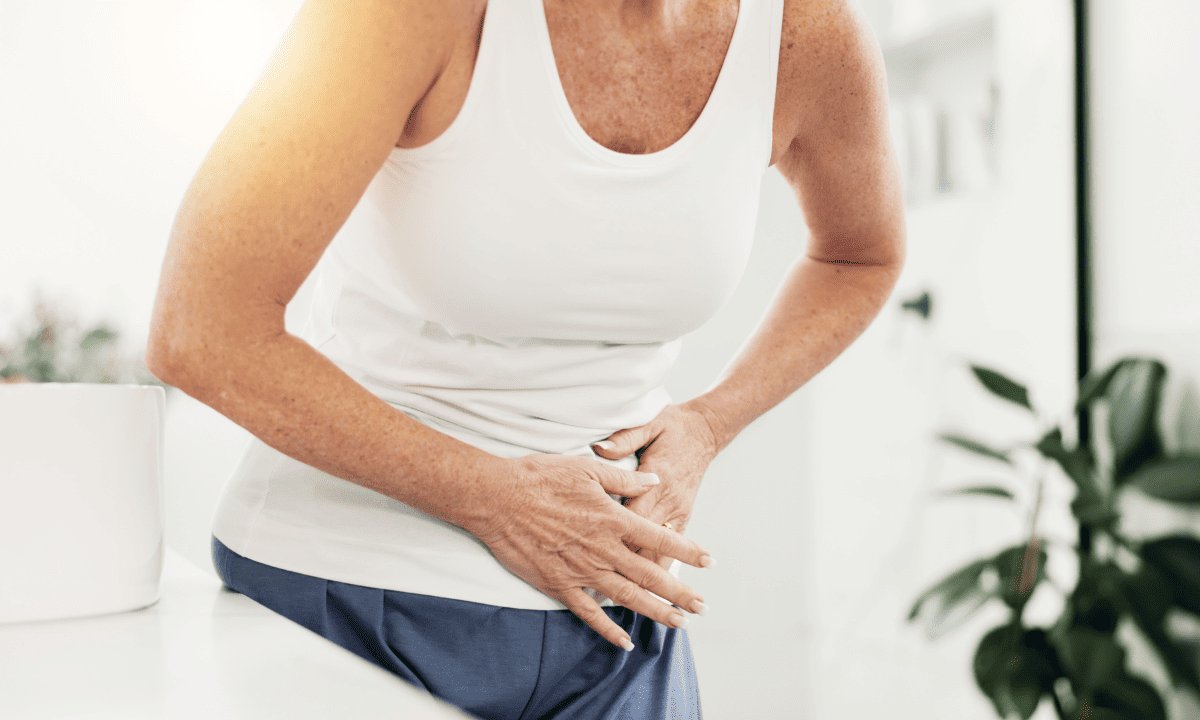 A woman in a white tank top leaning over and clutching her stomach in pain.
