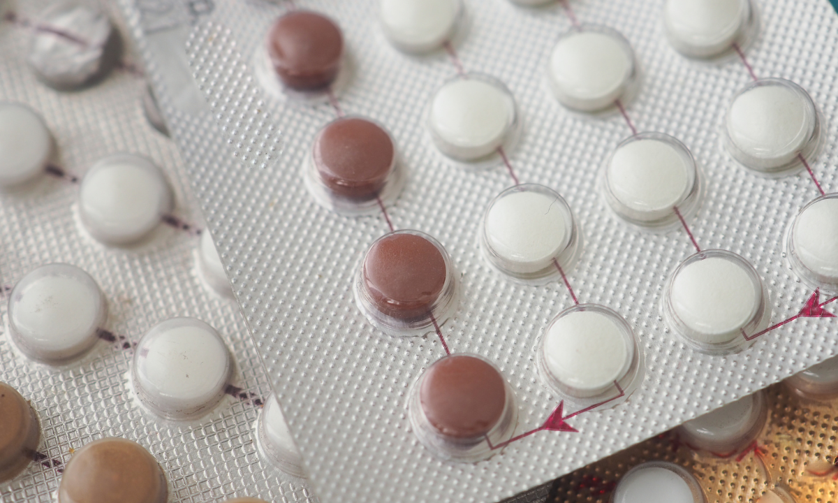 Close-up of several blister packs containing white and brown birth control pills.