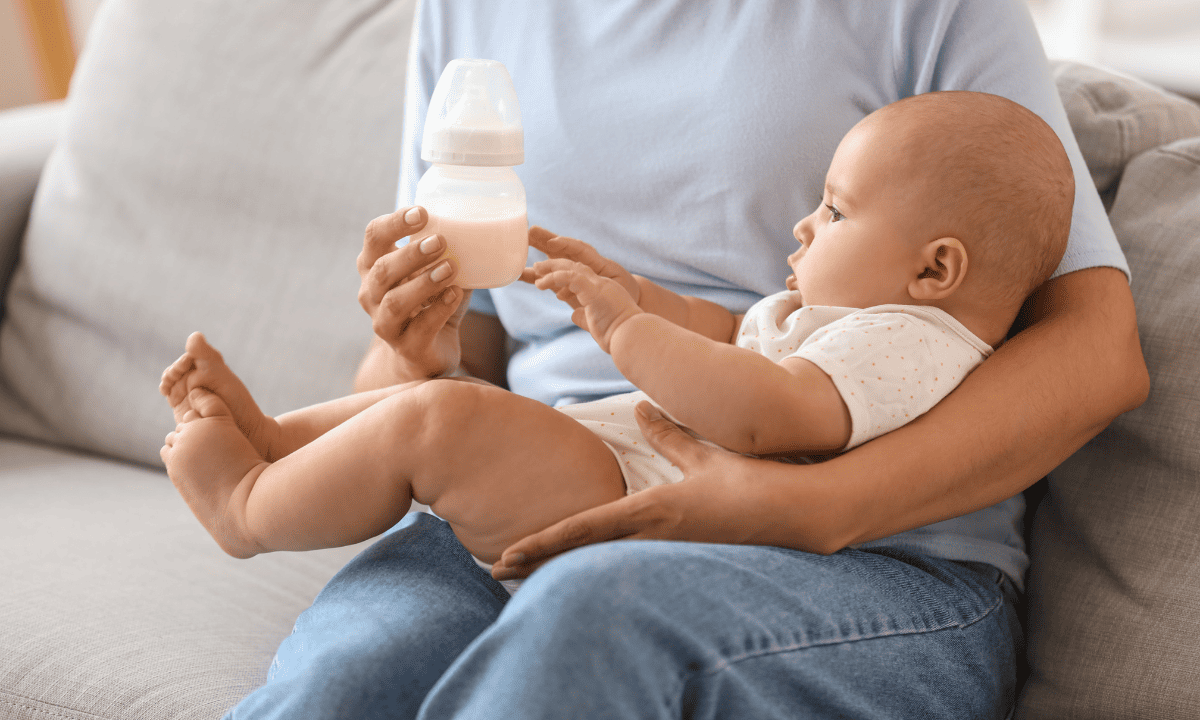 A mother holding her baby on her lap while holding up a bottle of milk.