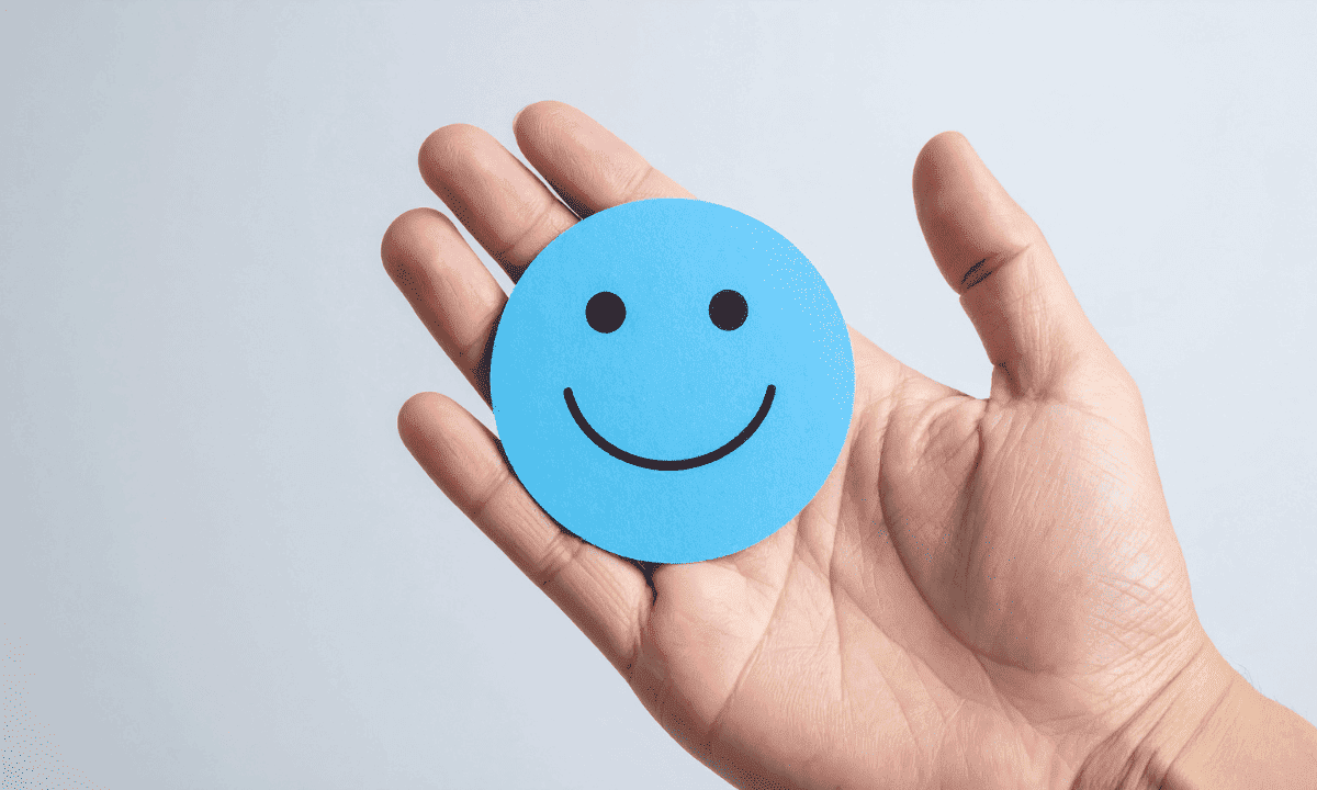 A person's open hand holding a small, light blue circular card with a simple, happy smiley face drawn on it.