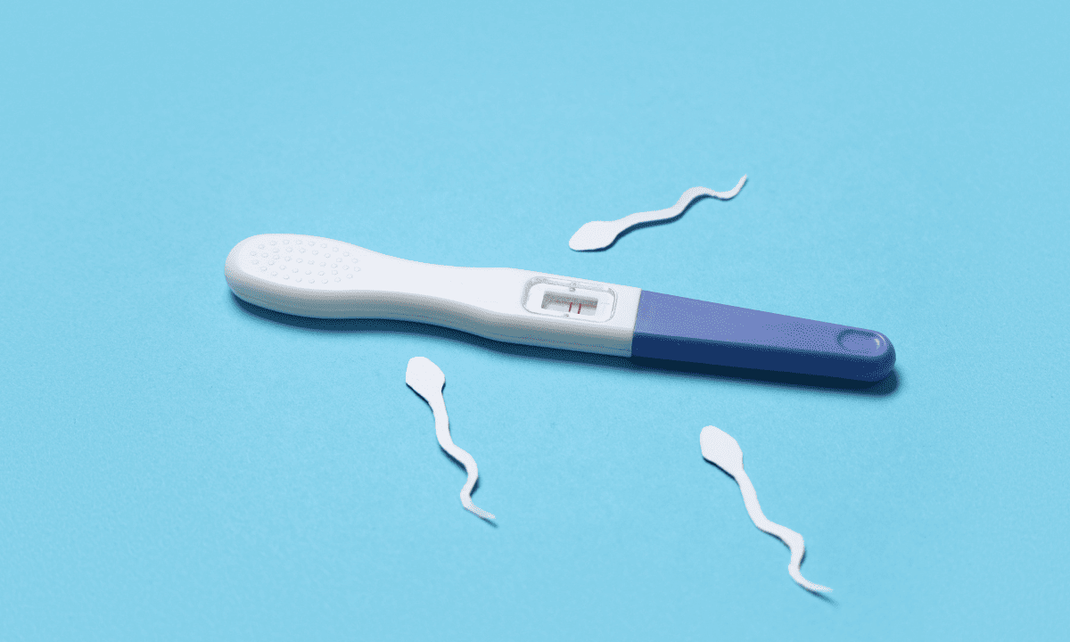 A positive pregnancy test showing two red lines, lying on a blue background surrounded by small paper cutouts of sperm