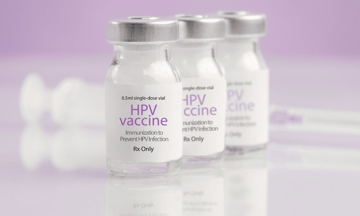 A close-up photo of three small glass vials labeled HPV Vaccine, Immunization to Prevent HPV Infection, set against a soft purple background.