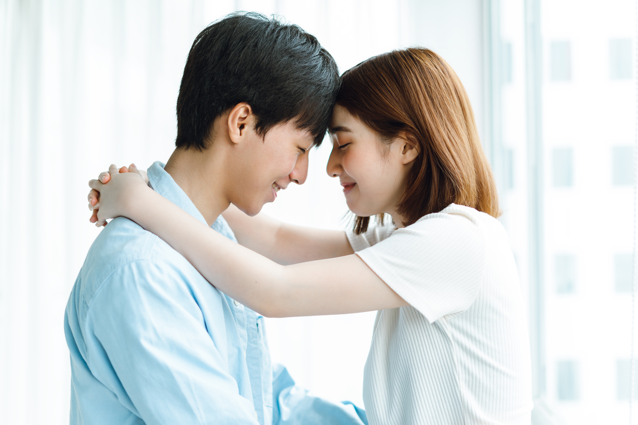 young asian couple putting heads together embracing and smiling