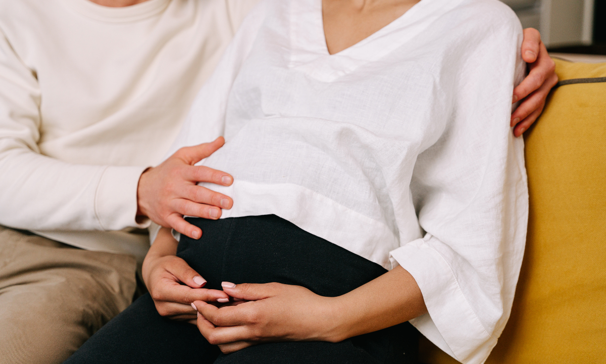 Close-up of a couple sitting together with their hands resting supportively on a pregnant belly.