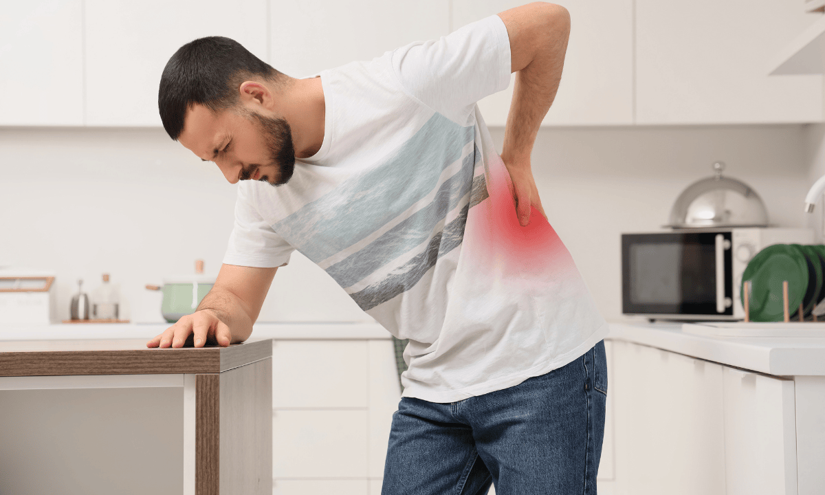 Man standing in a kitchen holding his lower back in pain