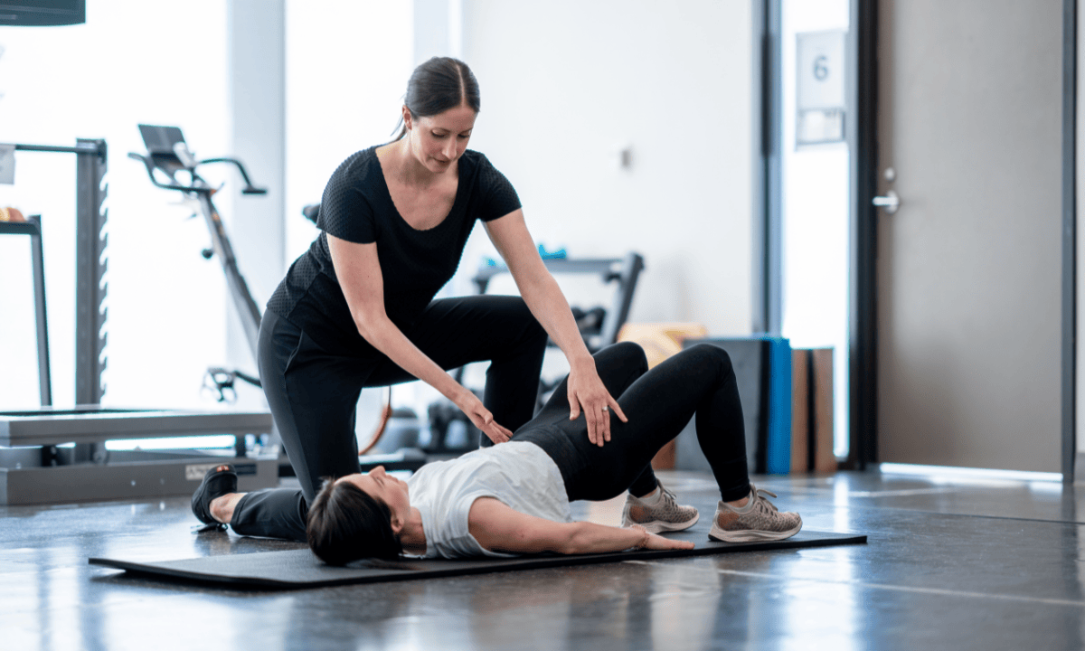 Physical therapist guiding woman through pelvic floor exercise on mat.