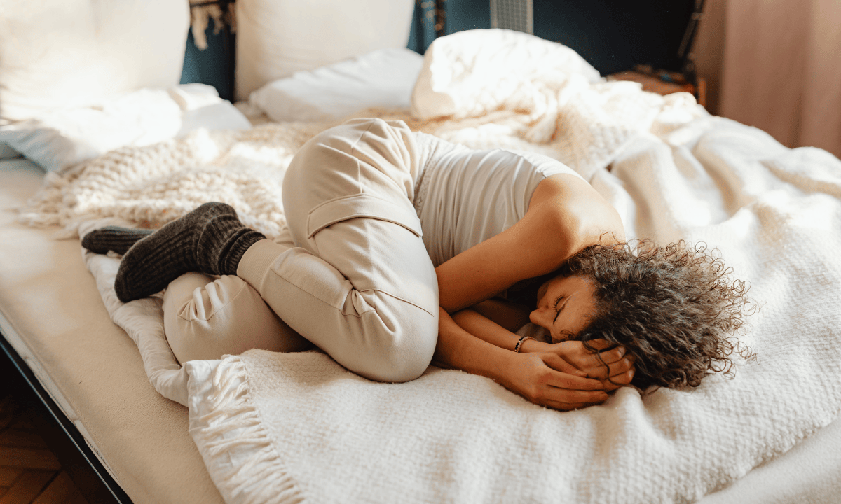 Woman curling tightly on white sheets