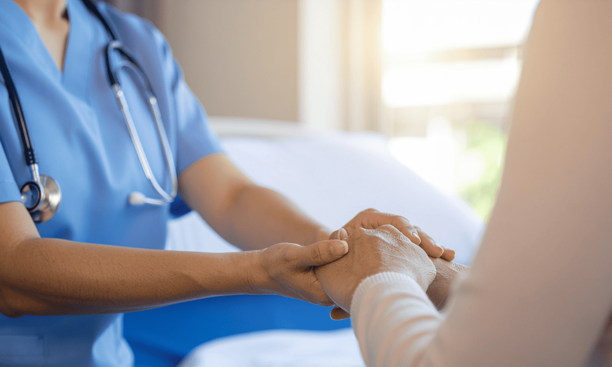 A close-up of a healthcare professional in blue scrubs gently holding a patient's hands to provide comfort and support.