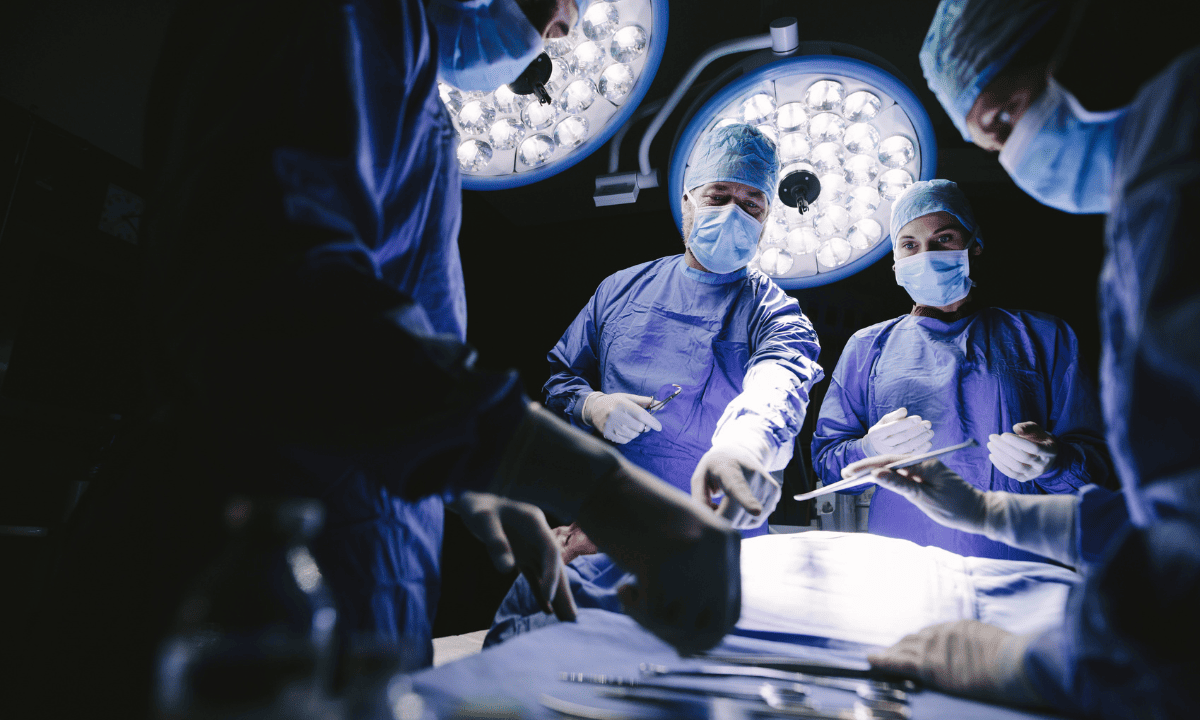 A team of surgeons in blue scrubs and masks performing a procedure under bright surgical lights in an operating room.