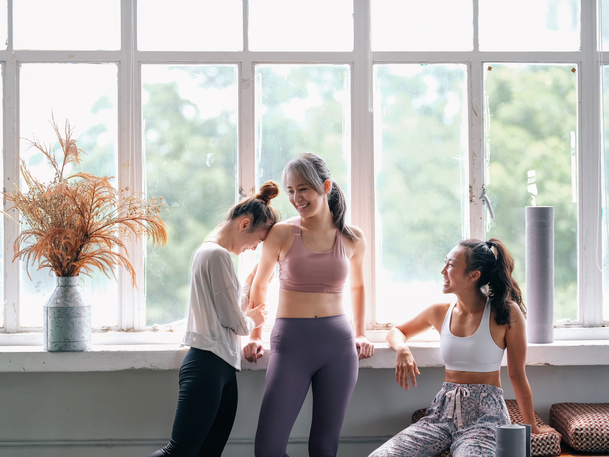 three young asian women in active wear athleisure talking an laughing after yoga or activity class