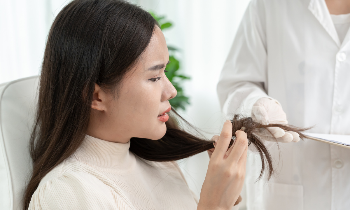 A woman looks concerned while a dermatologist examines her damaged hair ends during a clinic consultation.