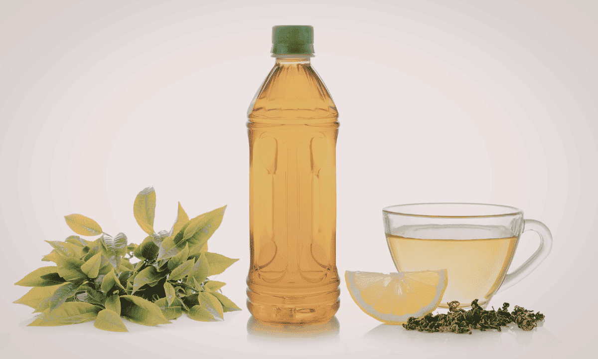 A bottle of tea tree oil shown with fresh tea tree leaves and a cup of tea with a lemon slice.