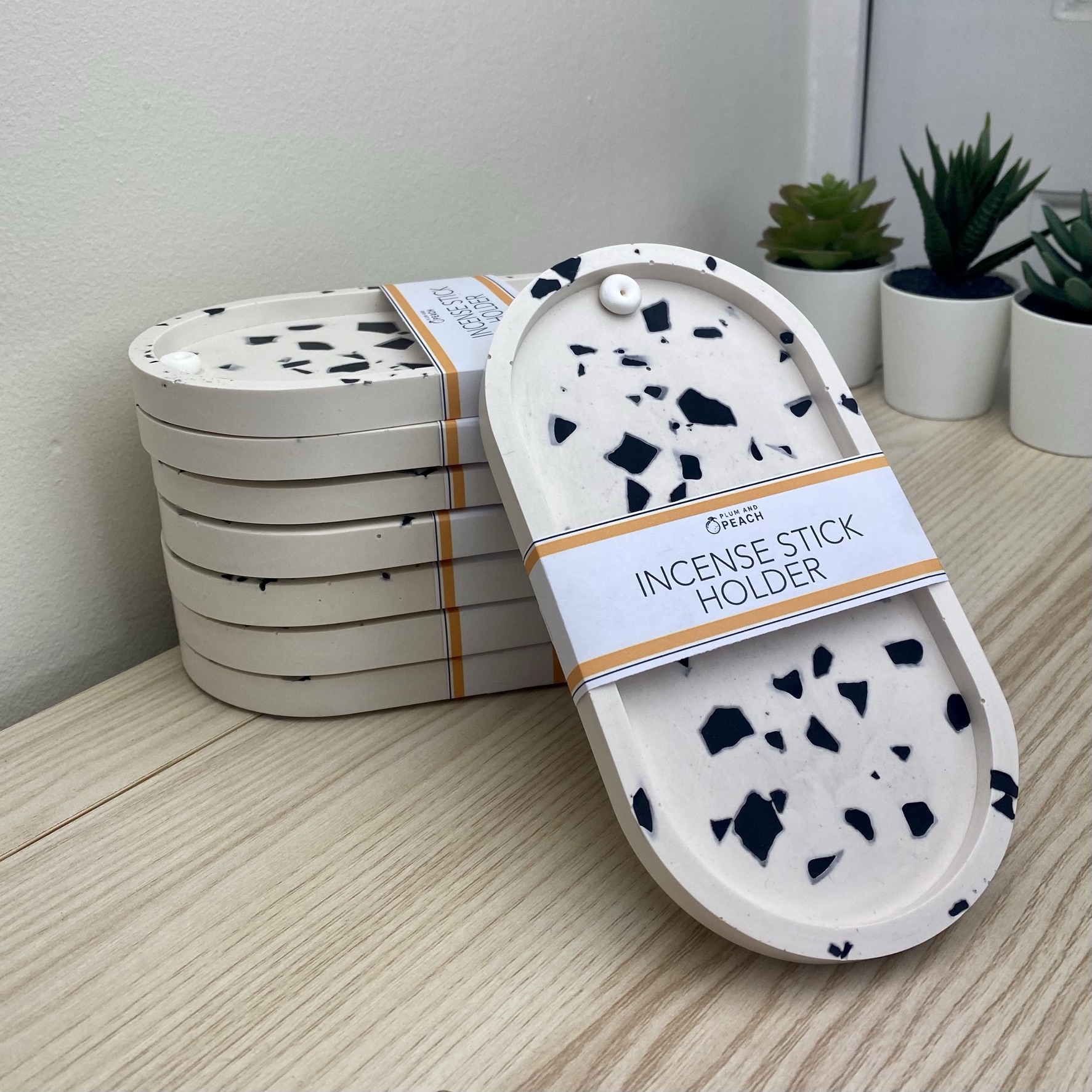 A Stack of white incense holders with black chips, on a light wood table with a white background