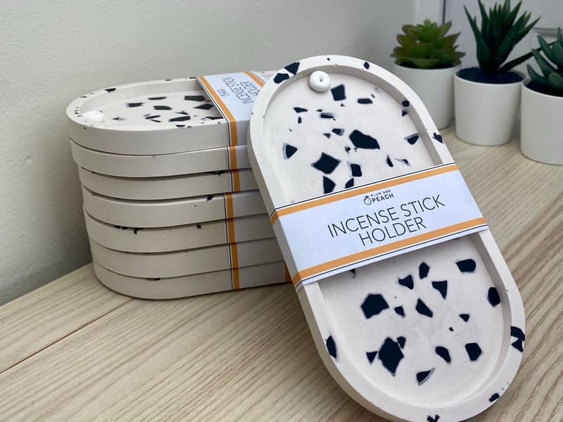 A Stack of white incense holders with black chips, on a light wood table with a white background