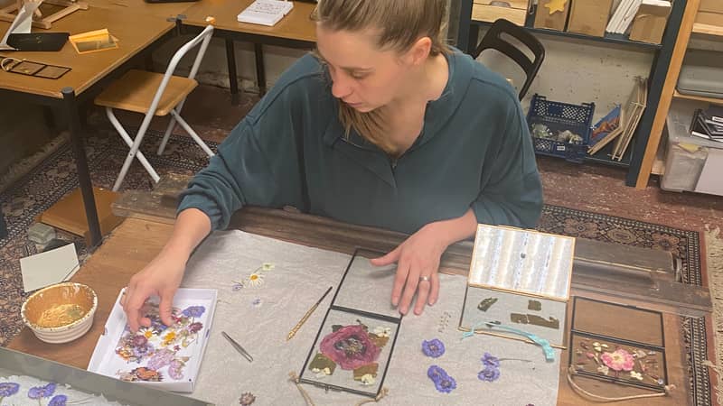 Elsker Creations studio with Sian working at her desk on a botanical artwork using pressed flowers and gold leaf