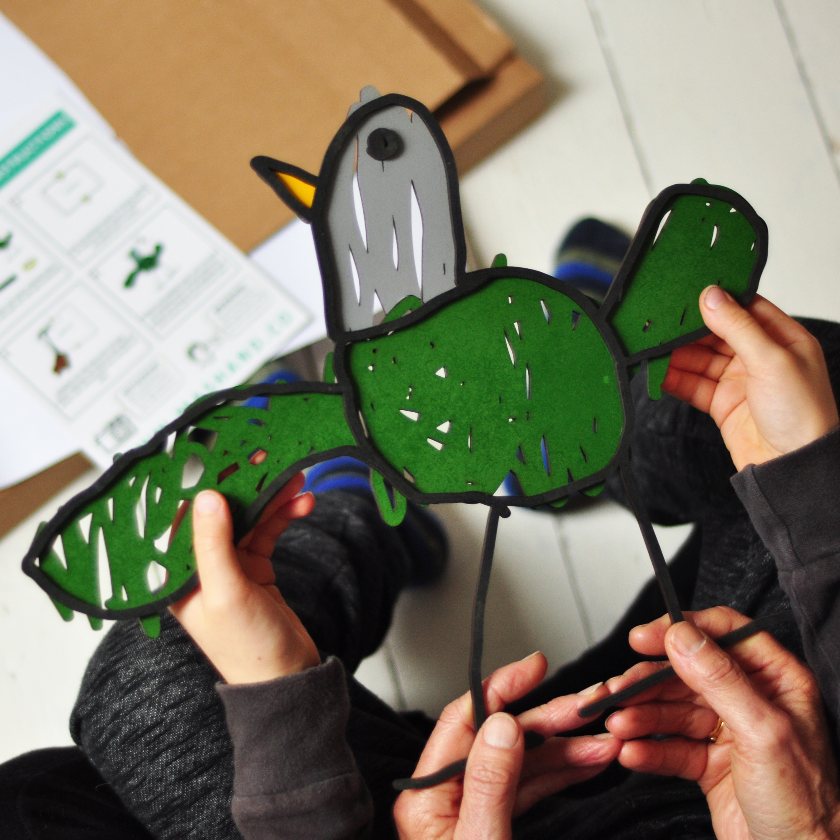 photograph of a laser cut drawing of a bird which is being held by two sets of hands. One set is a child and the other an adult
