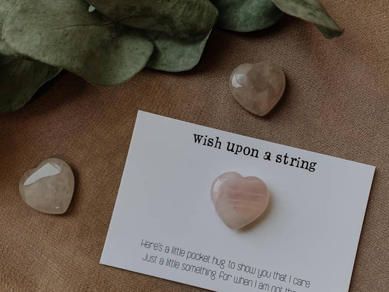 A Rose Quartz stone in the shape of a heart on a card with a motivational quote.