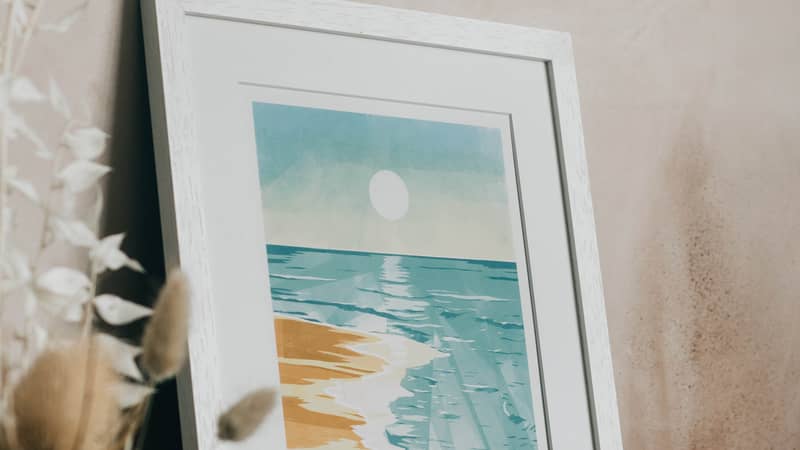 Framed print of a beach seascape at sunrise leaning against a wall.