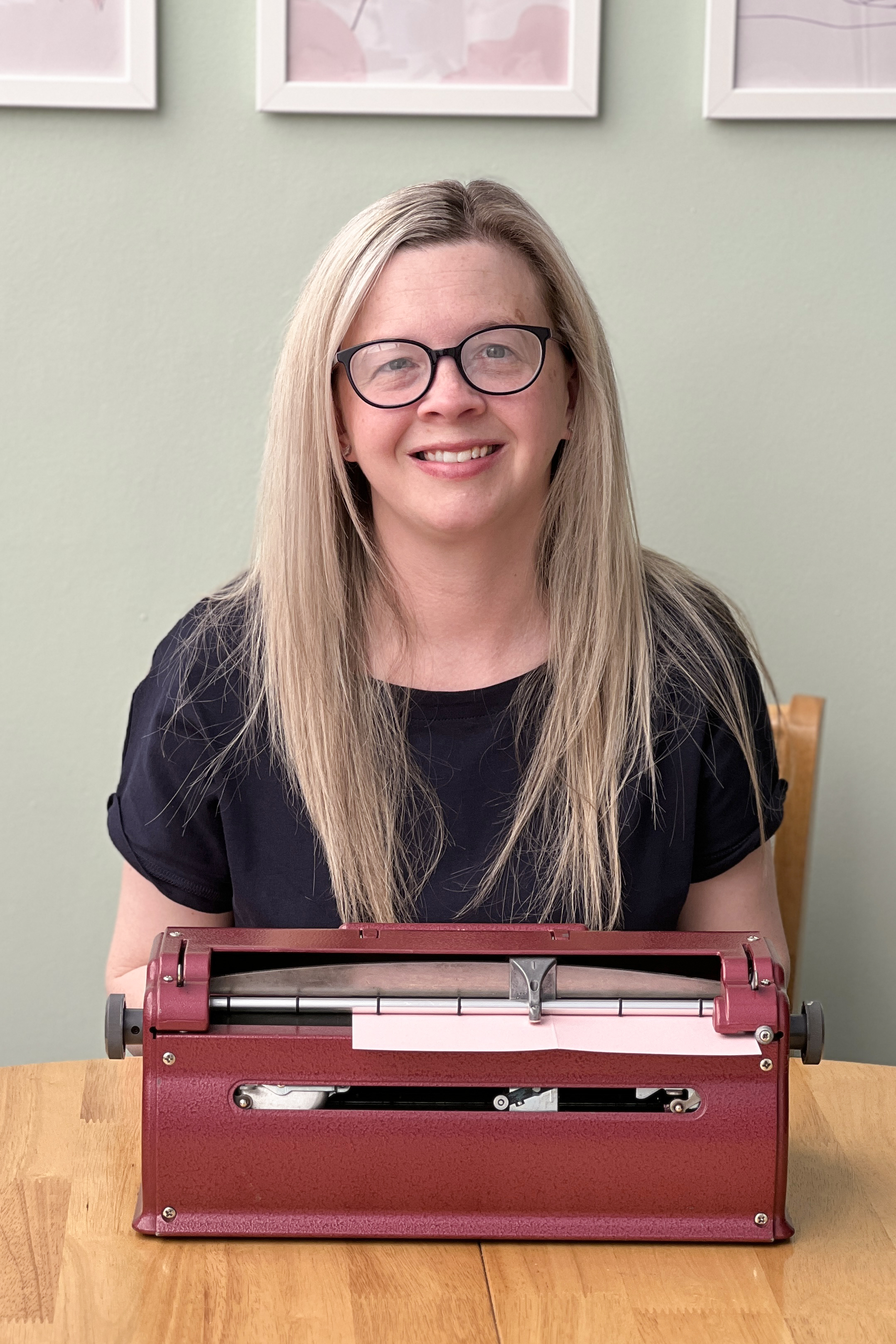 Hayley Kellard sat behind her Perkins brailler, she's wearing a navy blue t-shirt and her long hair is long and down.