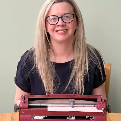 Hayley Kellard sat behind her Perkins brailler, she's wearing a navy blue t-shirt and her long hair is long and down.