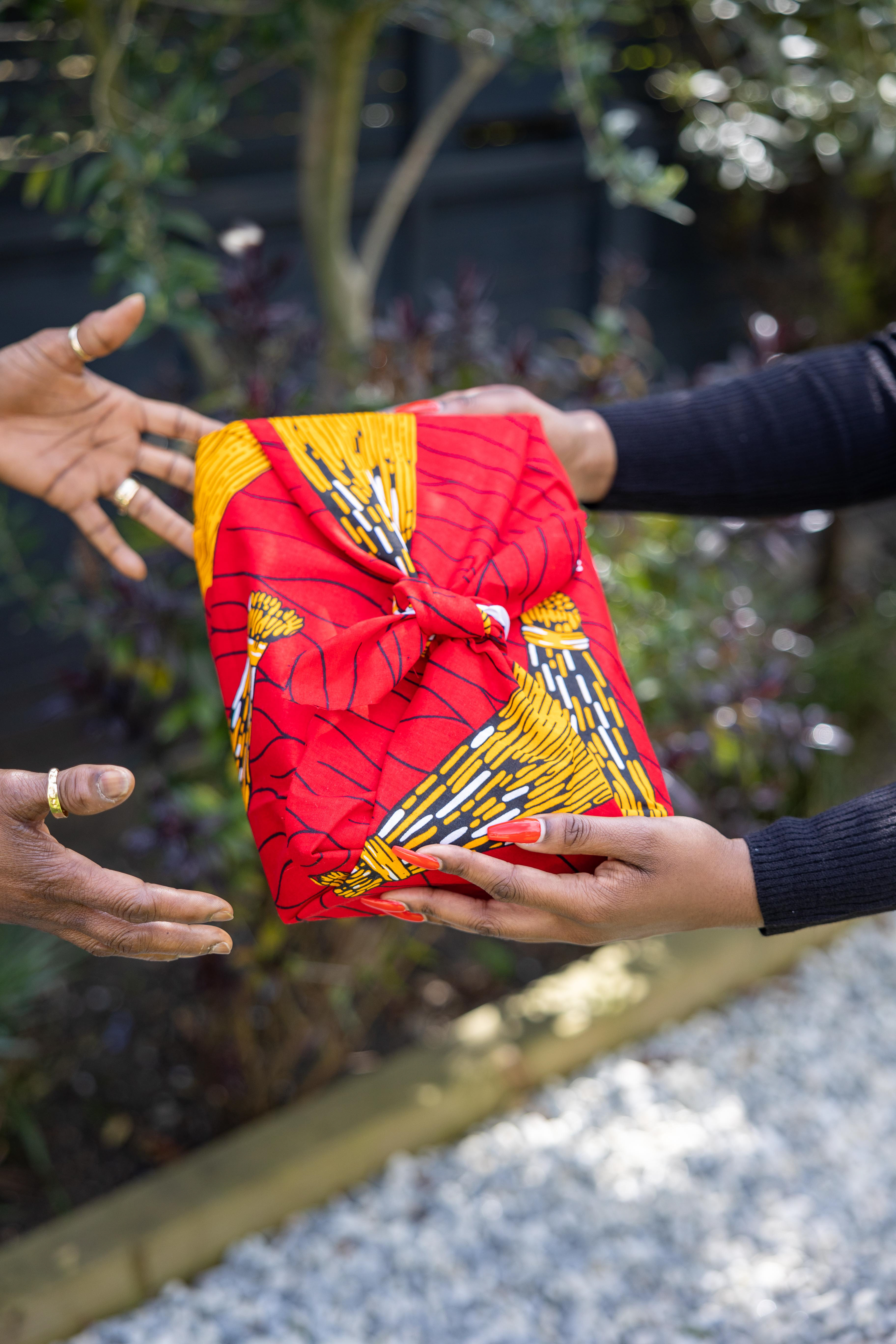 gifts wrapped in red african print fabric. black woman giving african inspired gift to her mother