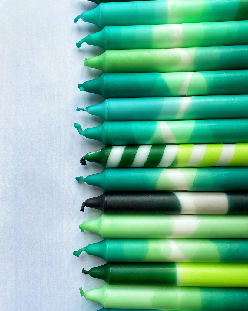 A selection of dip dyed candles in various shades of green.