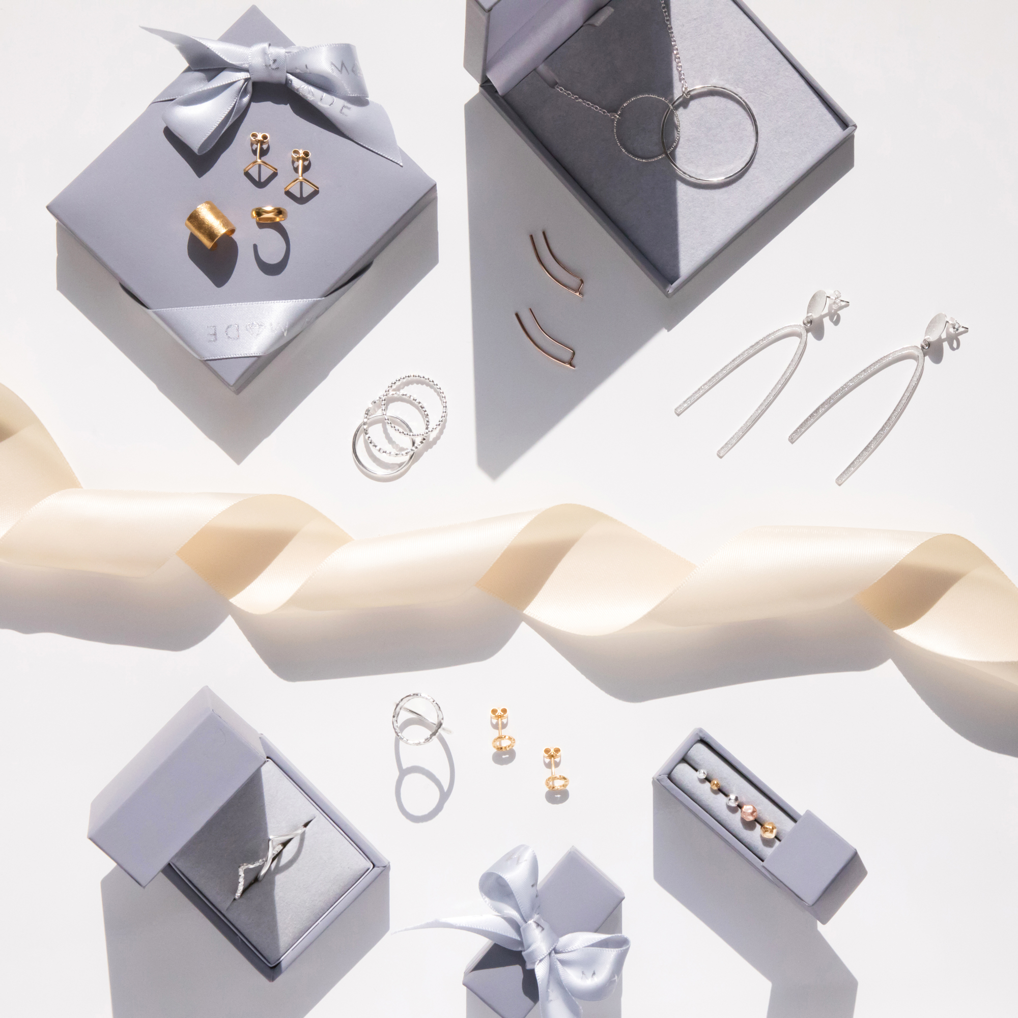 A selection of Marion Made Jewellery in gift boxes and layed flatwith a cream ribbon twisted along the middle