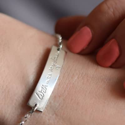 Close up of a silver bracelet with a curved bar which has handwriting engraved on it. The writing reads 'with all my love'.