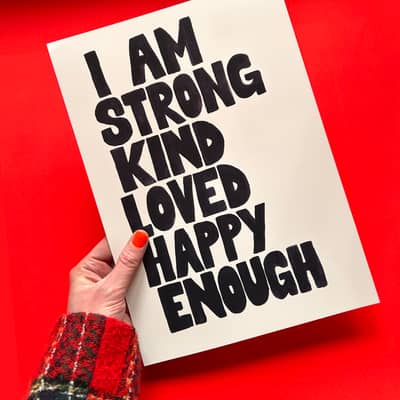 Hand holding typography print with positive affirmations on a red background