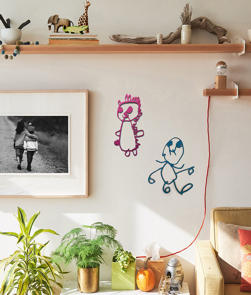 two pieces of laser cut art work are hanging on the wall of a livingroom. The art works are pink on the left and blue on the right.