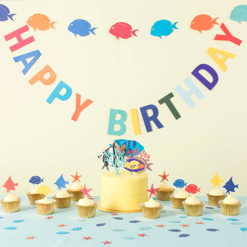 Under the Sea party decorations including paper fish garland, happy birthday bunting, tropical fish cake topper and table confetti