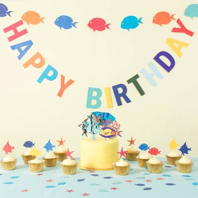 Under the Sea party decorations including paper fish garland, happy birthday bunting, tropical fish cake topper and table confetti