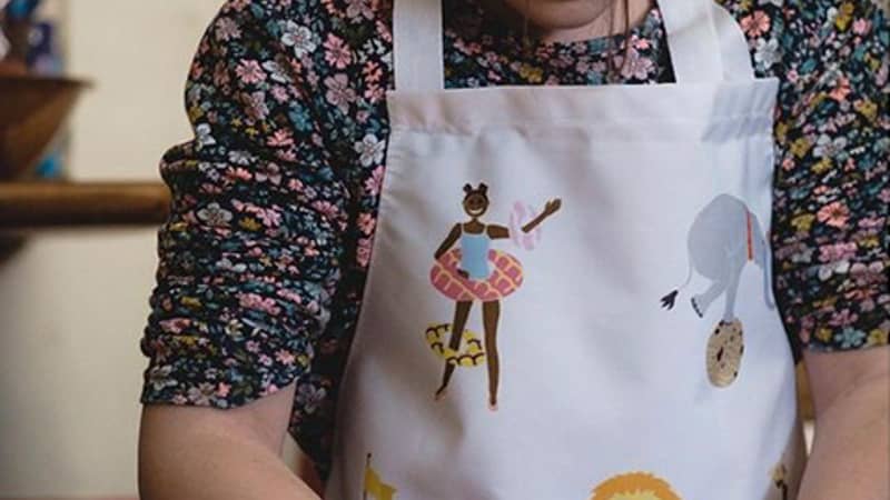 Young girl baking in the kitchen wearing a Hele Jelly Bean apron.