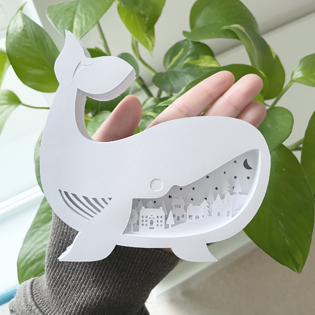 Whale lightbox with rural village cutout section. Held in with a plant as a daytime ornament.