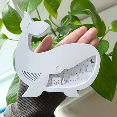 Whale lightbox with rural village cutout section. Held in with a plant as a daytime ornament.