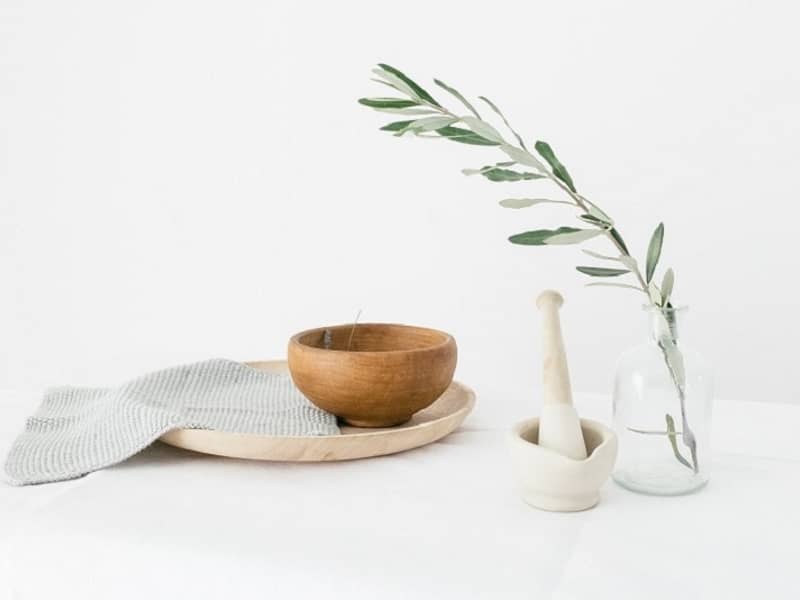 Olive branch, wooden bowl and pestle and mortar on a white table cloth