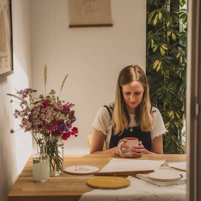 Becky sitting at table with fabric banners and flowers and cup of tea