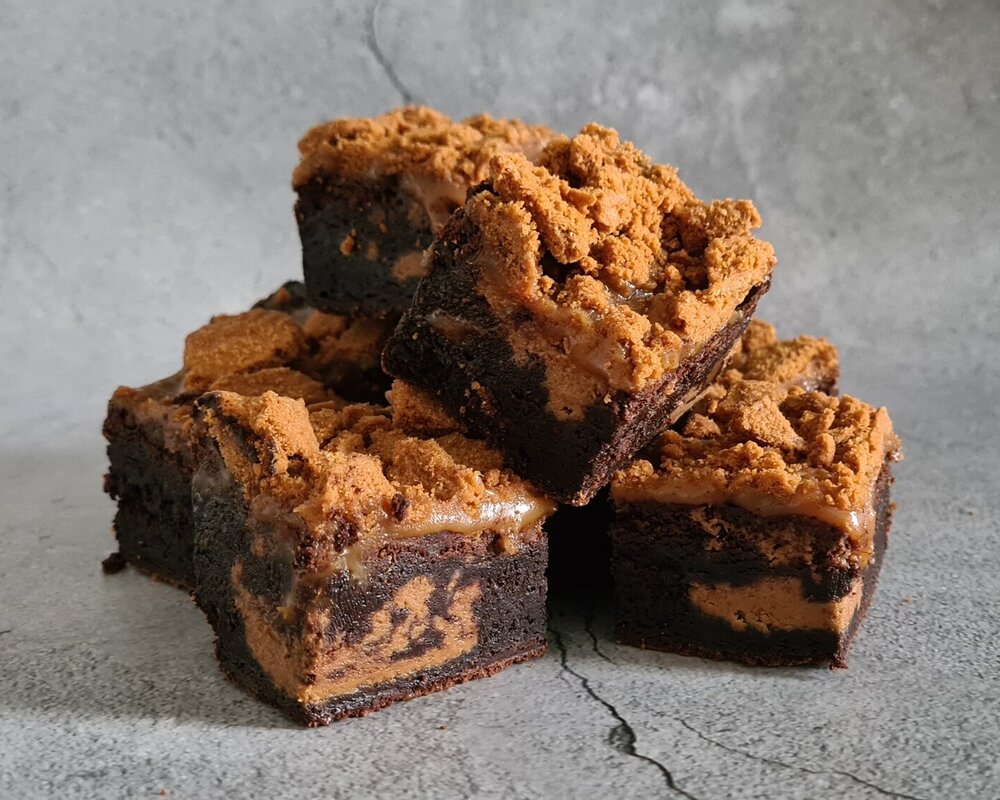 A stack of chocolate brownies, filled with Biscoff spread and covered in Biscoff biscuits and salted caramel