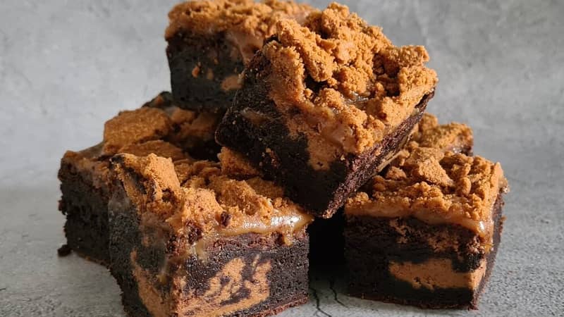 A stack of chocolate brownies, filled with Biscoff spread and covered in Biscoff biscuits and salted caramel