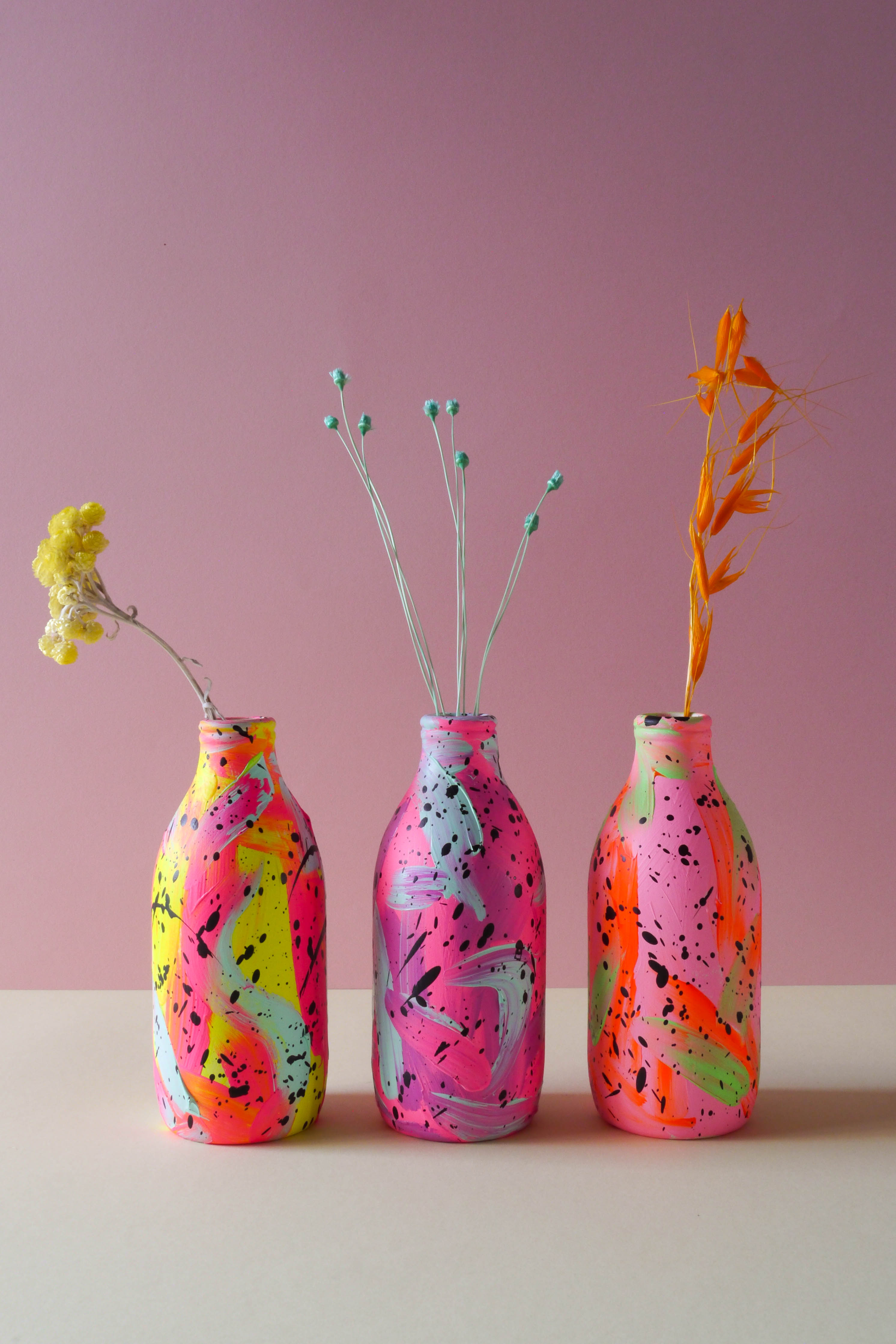 Three brightly coloured hand painted ceramic vases displayed in a row with dried flowers
