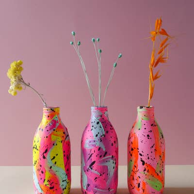 Three brightly coloured hand painted ceramic vases displayed in a row with dried flowers