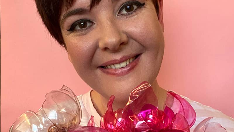 Aimee smiling against a pink background holding a big bunch of hot pink recycled plastic bottle flowers