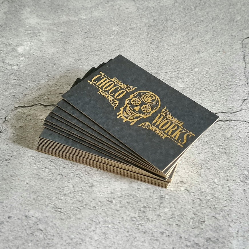 A stack of black business cards on a stone-grey background. The business cards include gold-foil edges and gold-foil logo