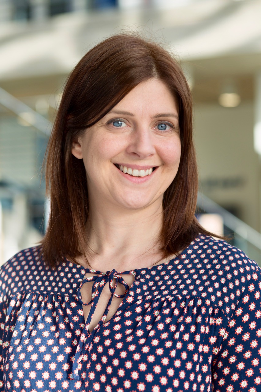 Portrait picture of KindlyYarn founder, wearing navy patterned dress, brown hair, blurred background