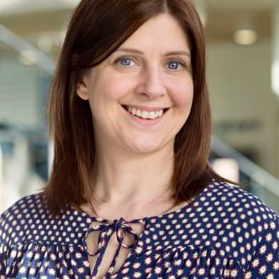 Portrait picture of KindlyYarn founder, wearing navy patterned dress, brown hair, blurred background