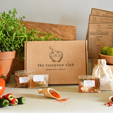 A Teaspoon Club box is front and centre with spice packets displayed around it, as well as fresh chillies and oregano
