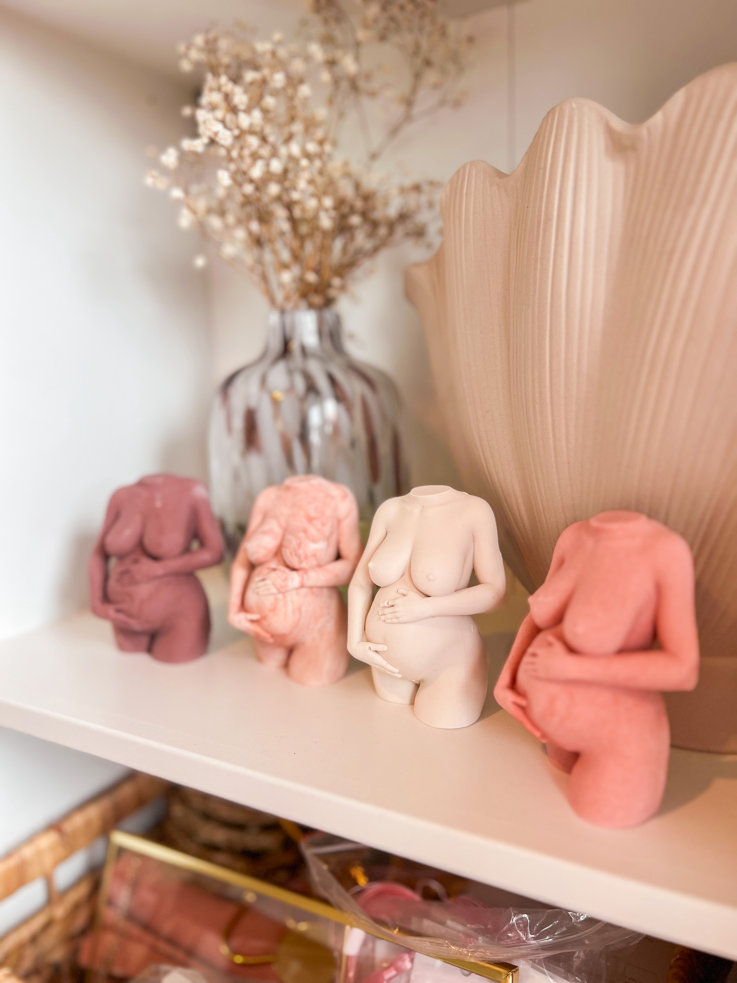 Four statues of pregnant women holding their stomachs, the same design in different colours